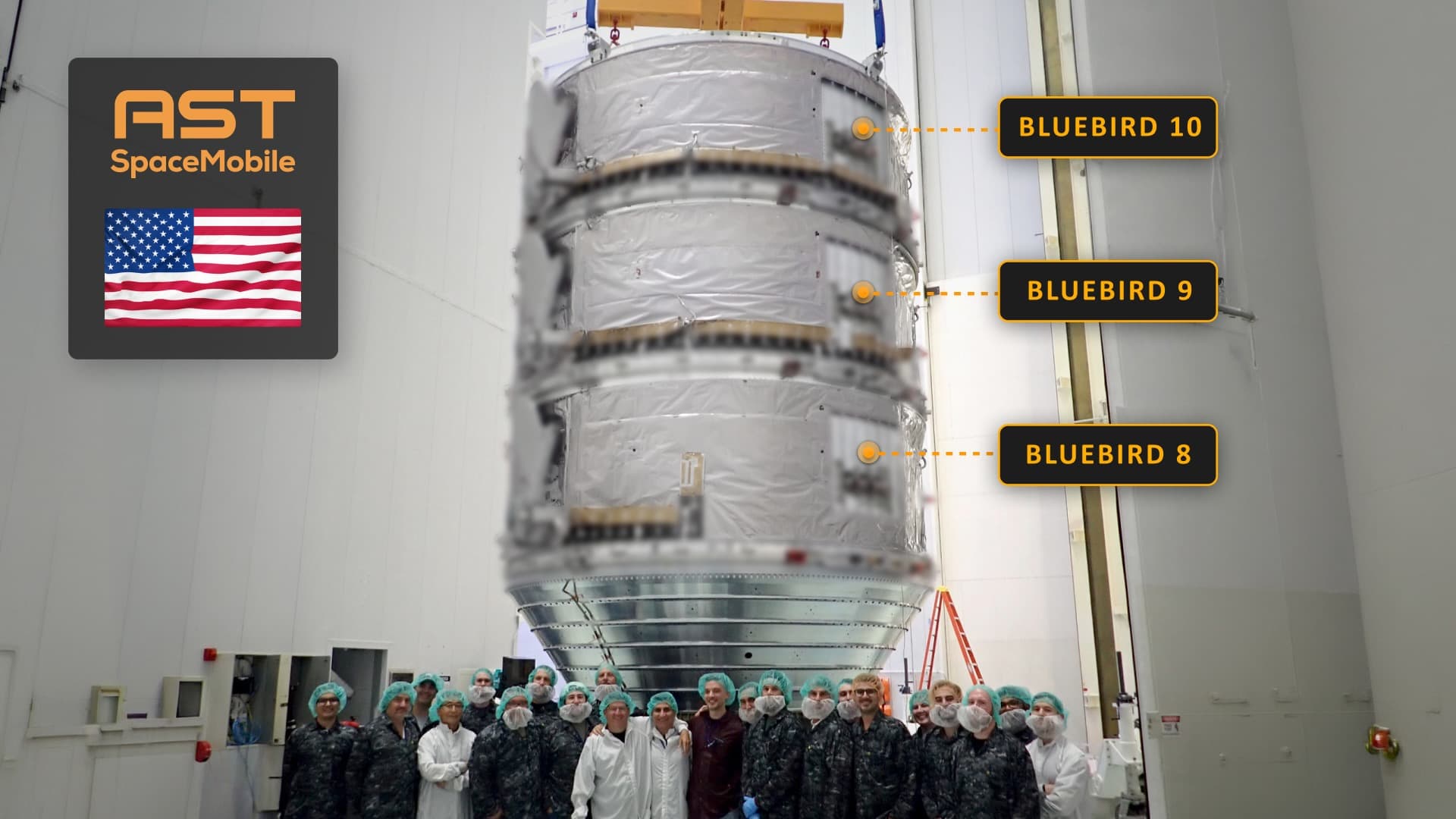 several dozen people stand in front of a stack of three large satellites inside a large, white-walled room