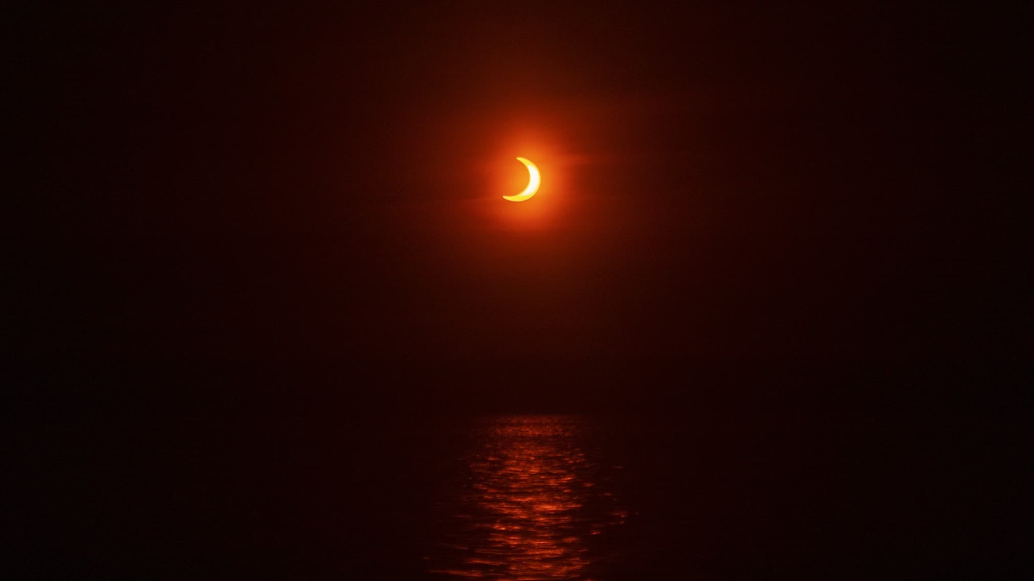 eclipse occurring near sunset the crescent sun glows with a vibrant orange hue