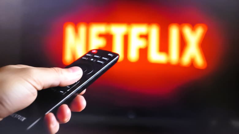 Closeup of a hand using a remote control to navigate Netflix
