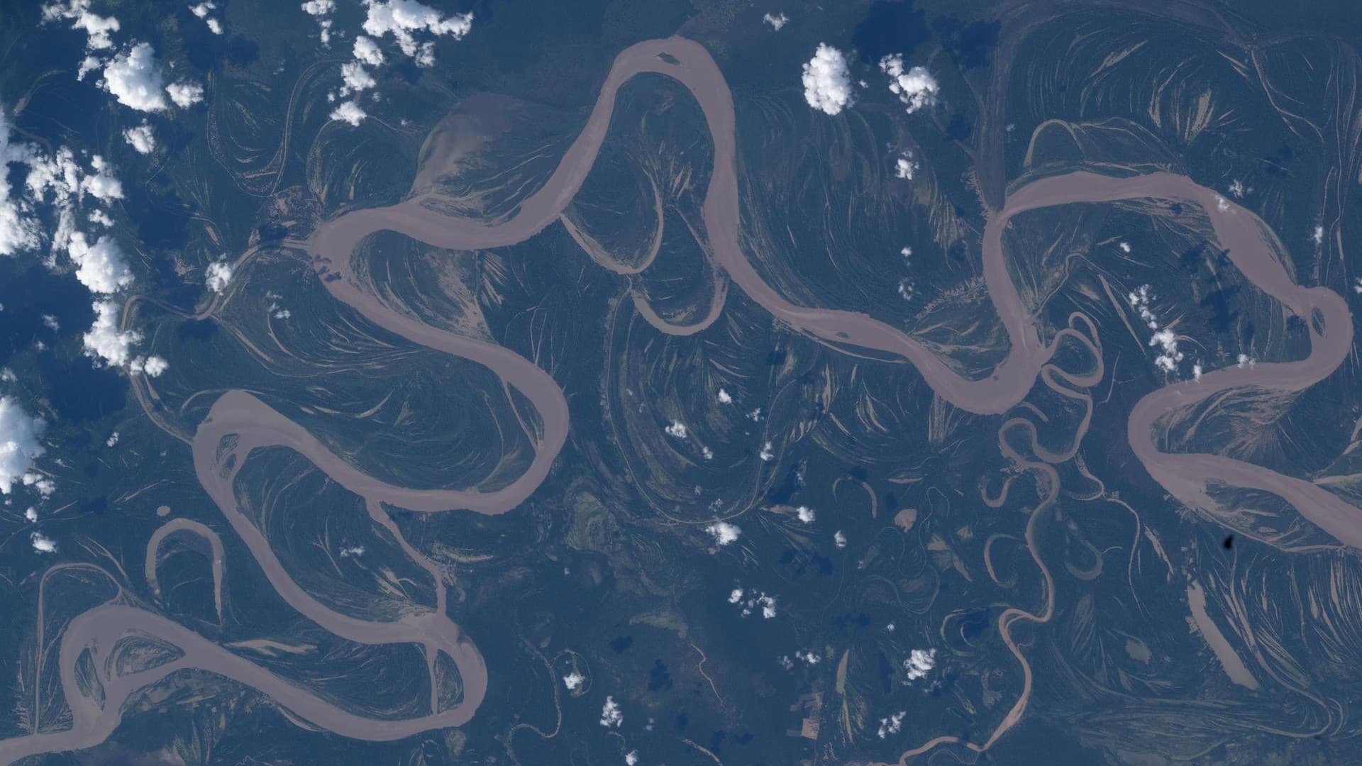 An image of the Ucayali River taken from space shows the river snaking in a light brown color across dark blue and green land with some small fluffy white clouds overhead.