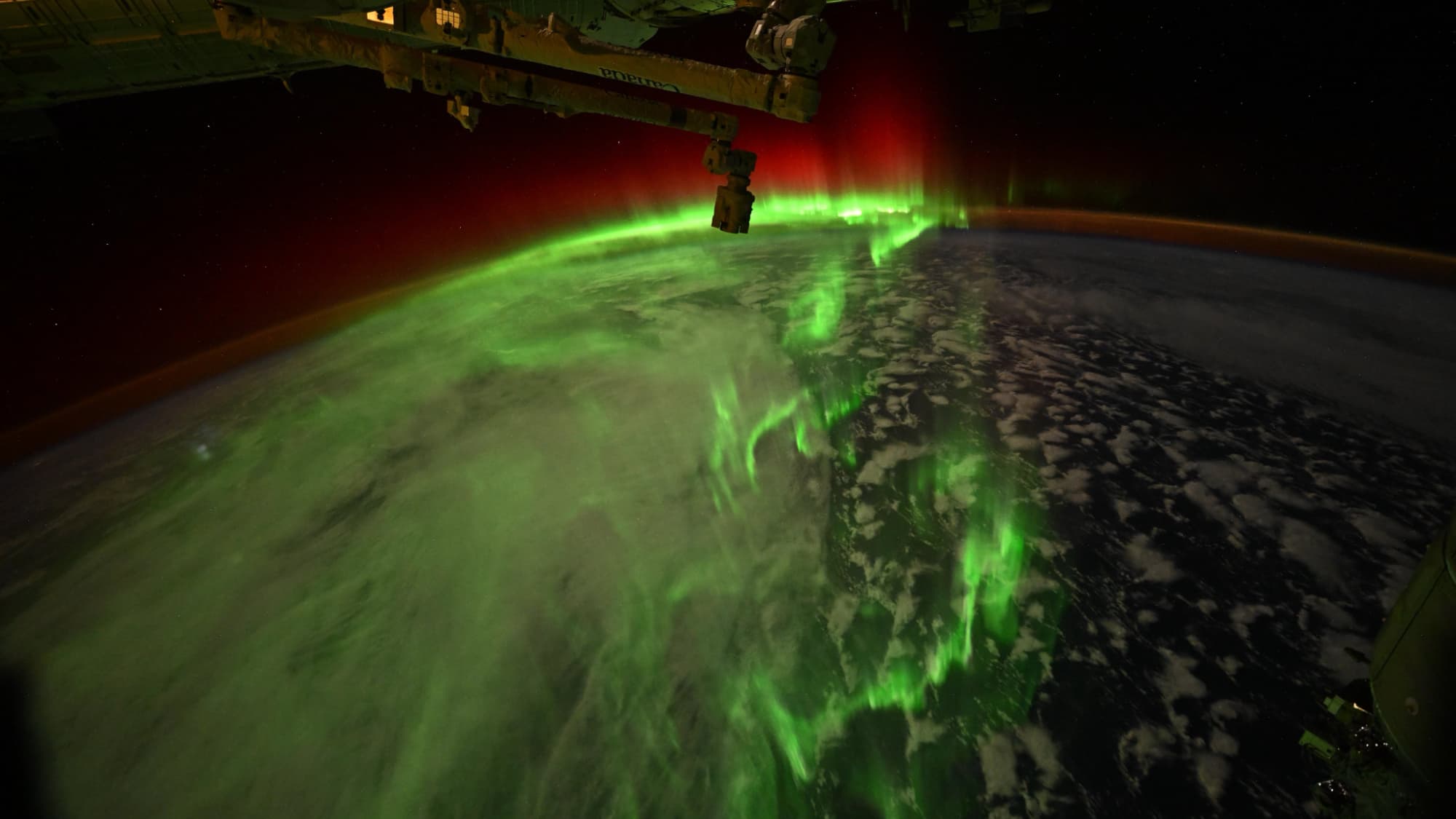 Bright green and red auroras over Earth as seen from space.