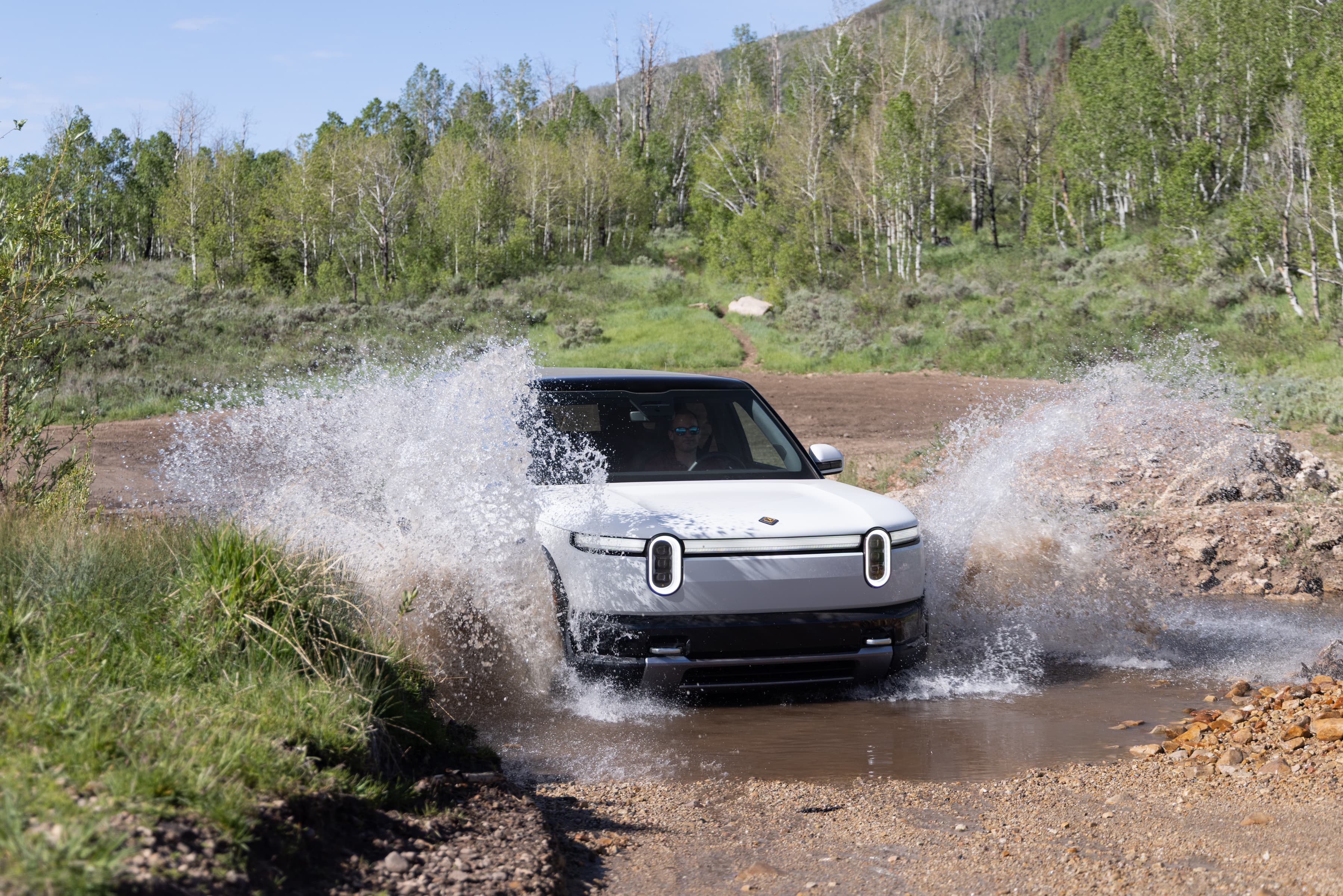A white Rivian R2 splashes through a stream