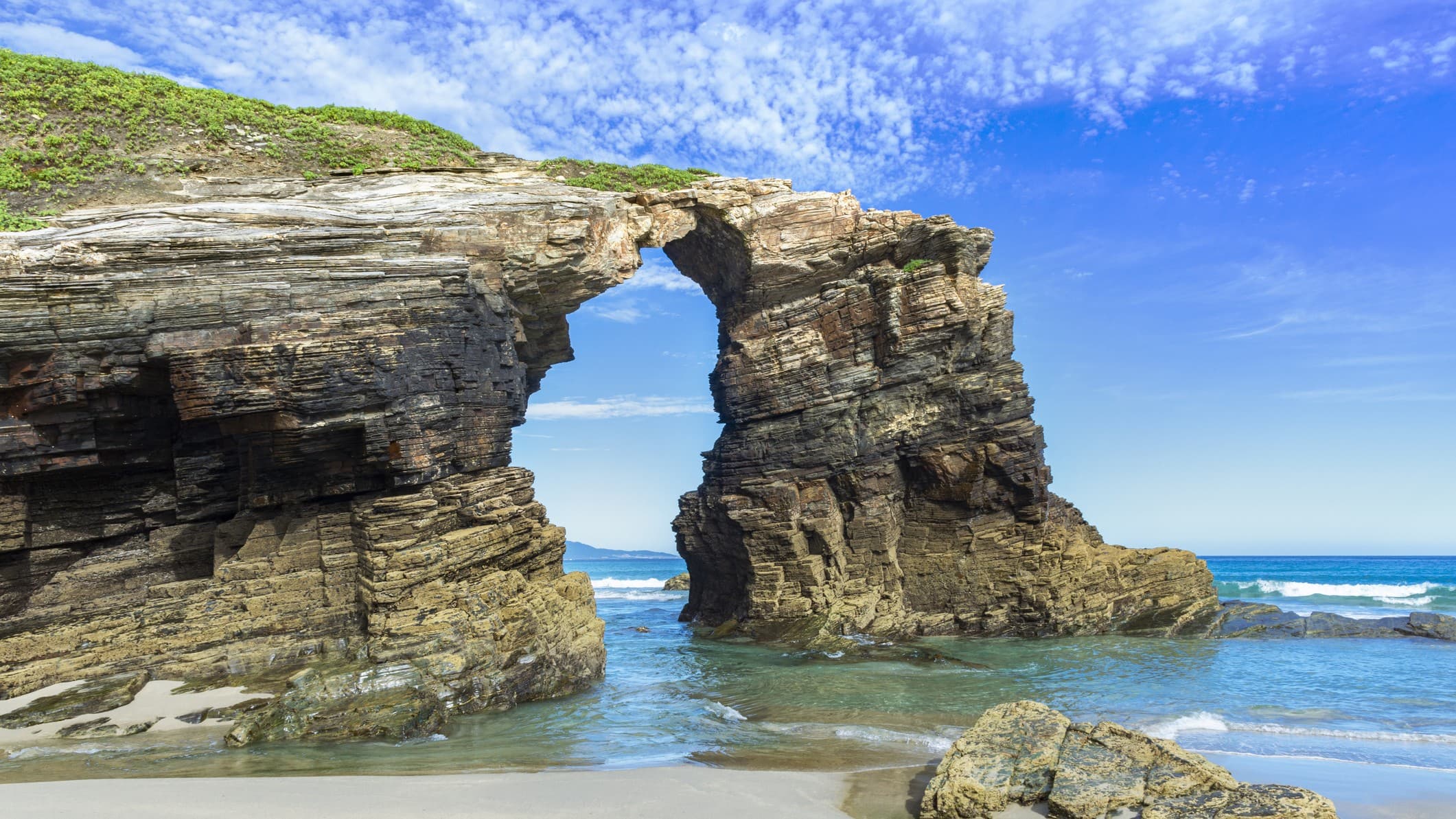 impressive looking rock structure in the shape of an arch. deep blue sky above and light blue waters below.