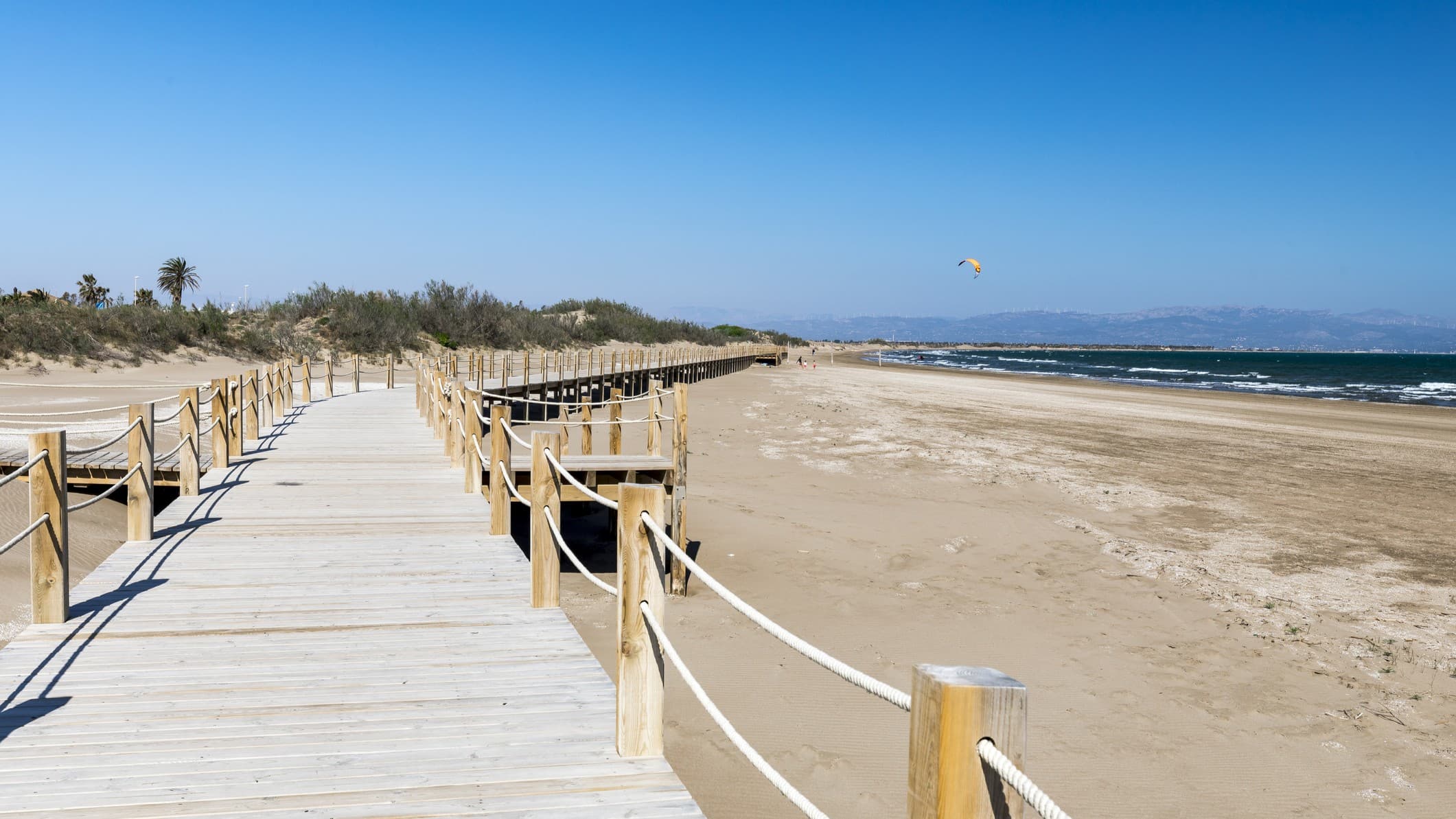 sandy beach with a wooden boardwalk stretching into the distance. The sky and ocean are a deep blue.