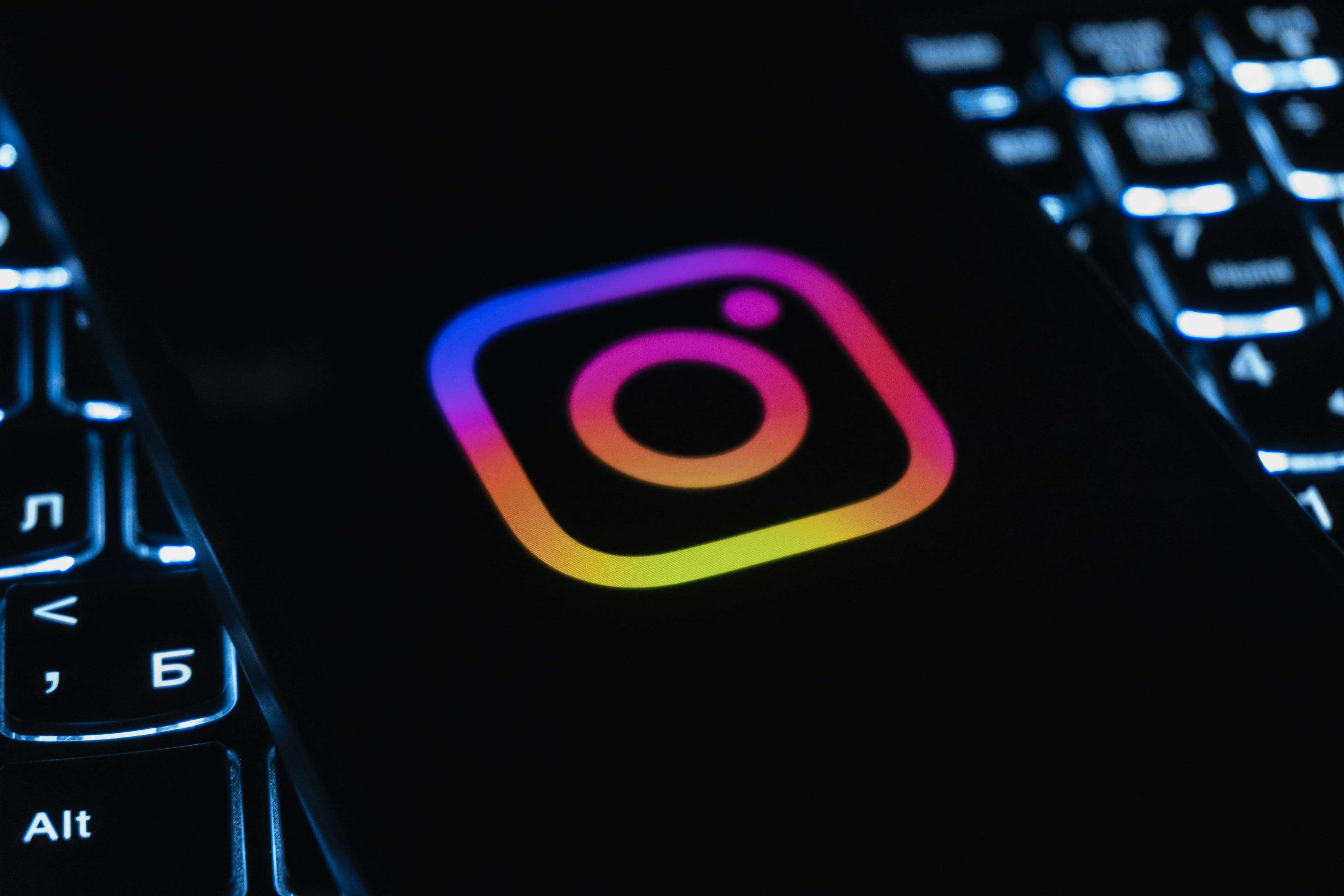 a photo of Instagram's logo on a phone on a darkened background featuring a lit-up keyboard