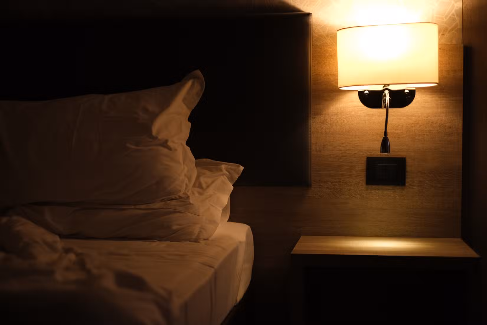 Beside lamp emitting soft, warm light on the bed.