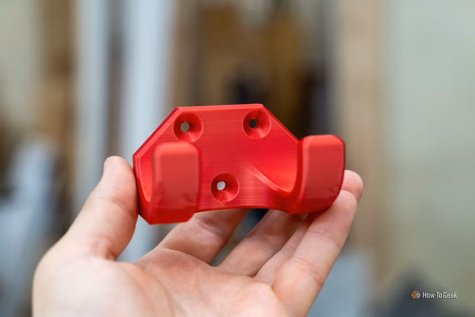 Red 3D printed wall hook for shop organization held in hand.