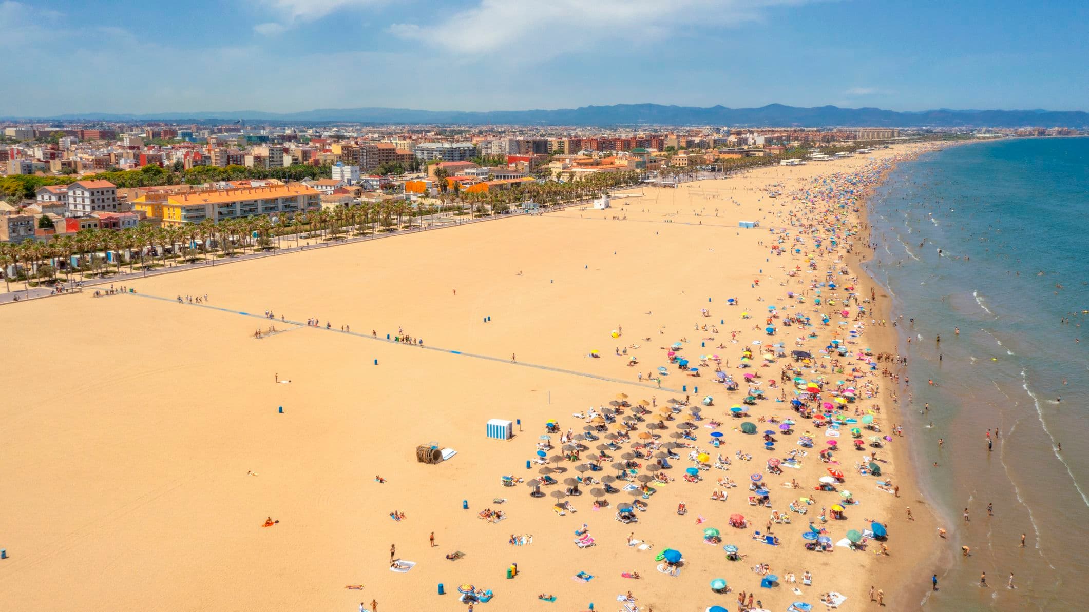 golden sandy beach stretching far into the distance, people are peppered along the shoreline with parasols and beach towels.