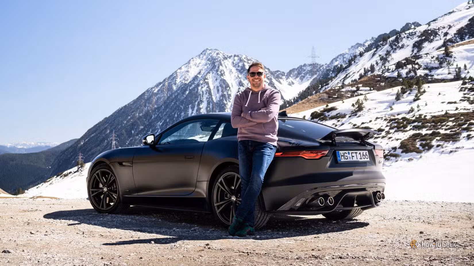 Static rear 3/4 shot of a black 2023 Jaguar F-Type R 75 with a man posing beside it.