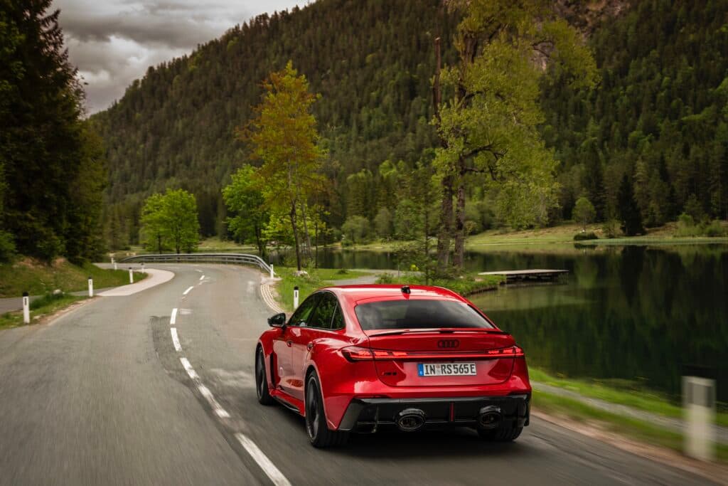 A red Audi RS5 drives past a lake