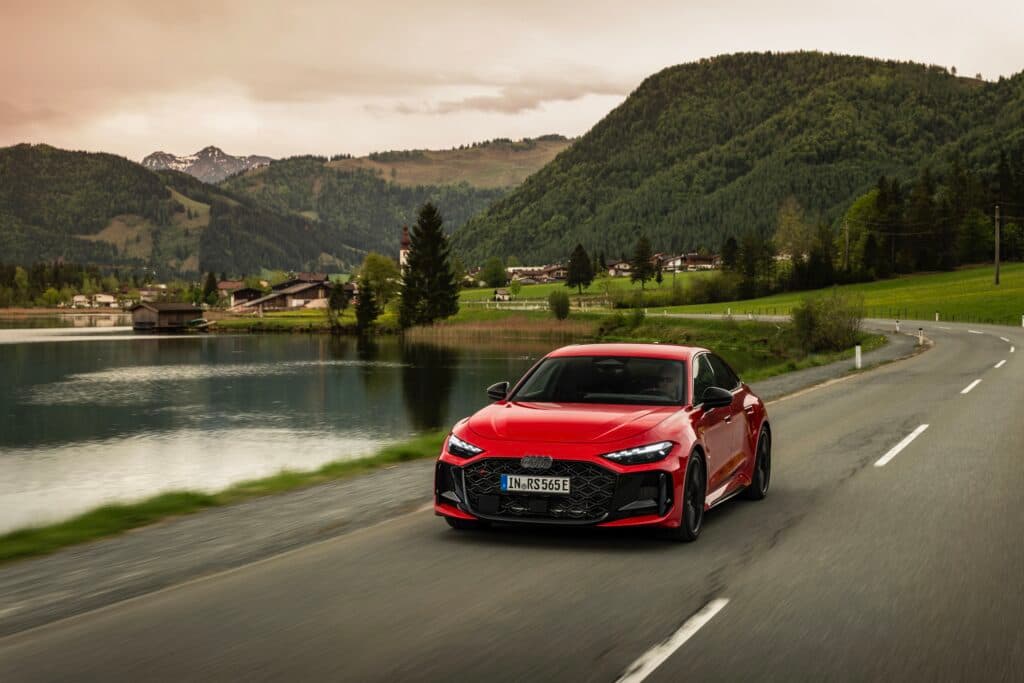 A red Audi RS5 drives past a lake