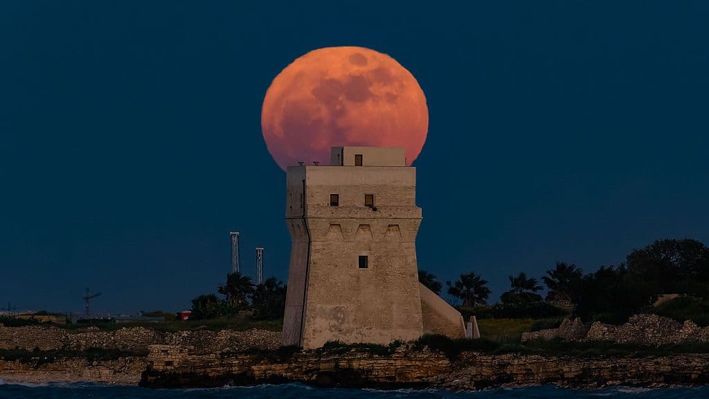 a vibrant orange full moon behind a large stone tower.