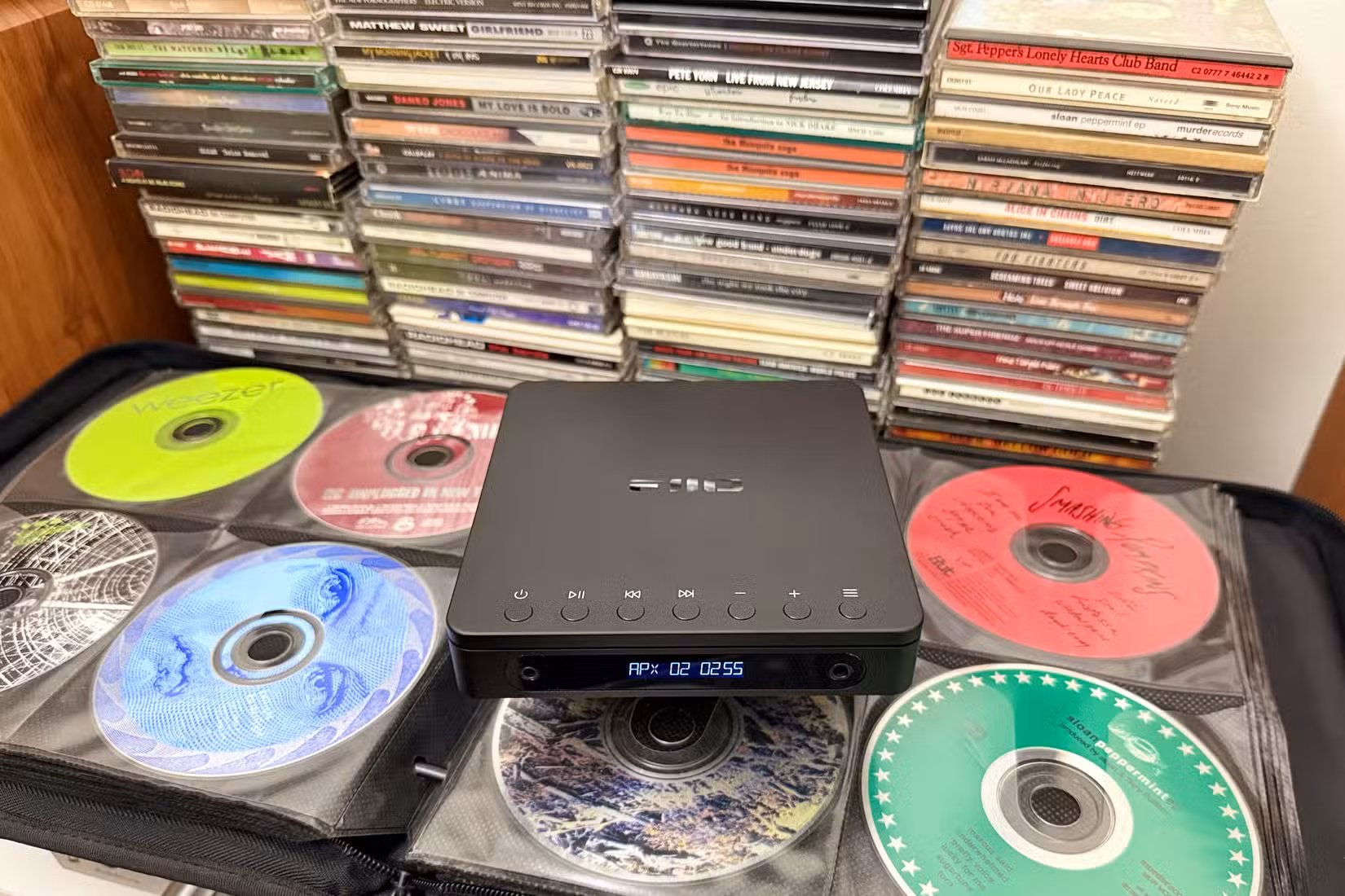A CD walkman with an open CD binder and CDs stacked behind.