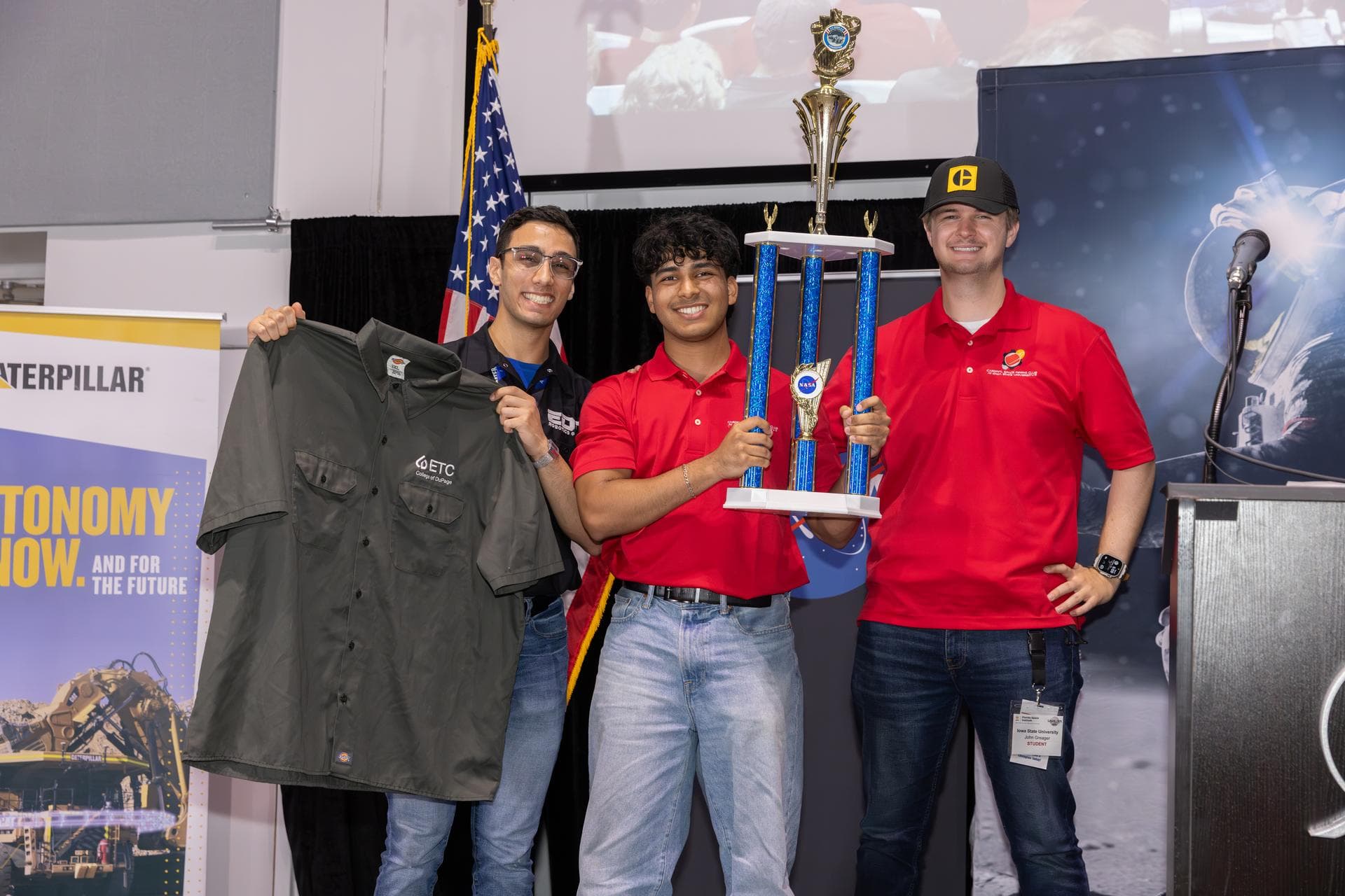 Three college students hold up a trophy and shirt