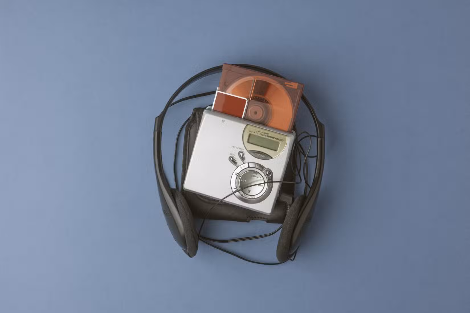 Portable MiniDisc player with a disc inserted, surrounded by wired headphones on a blue background.