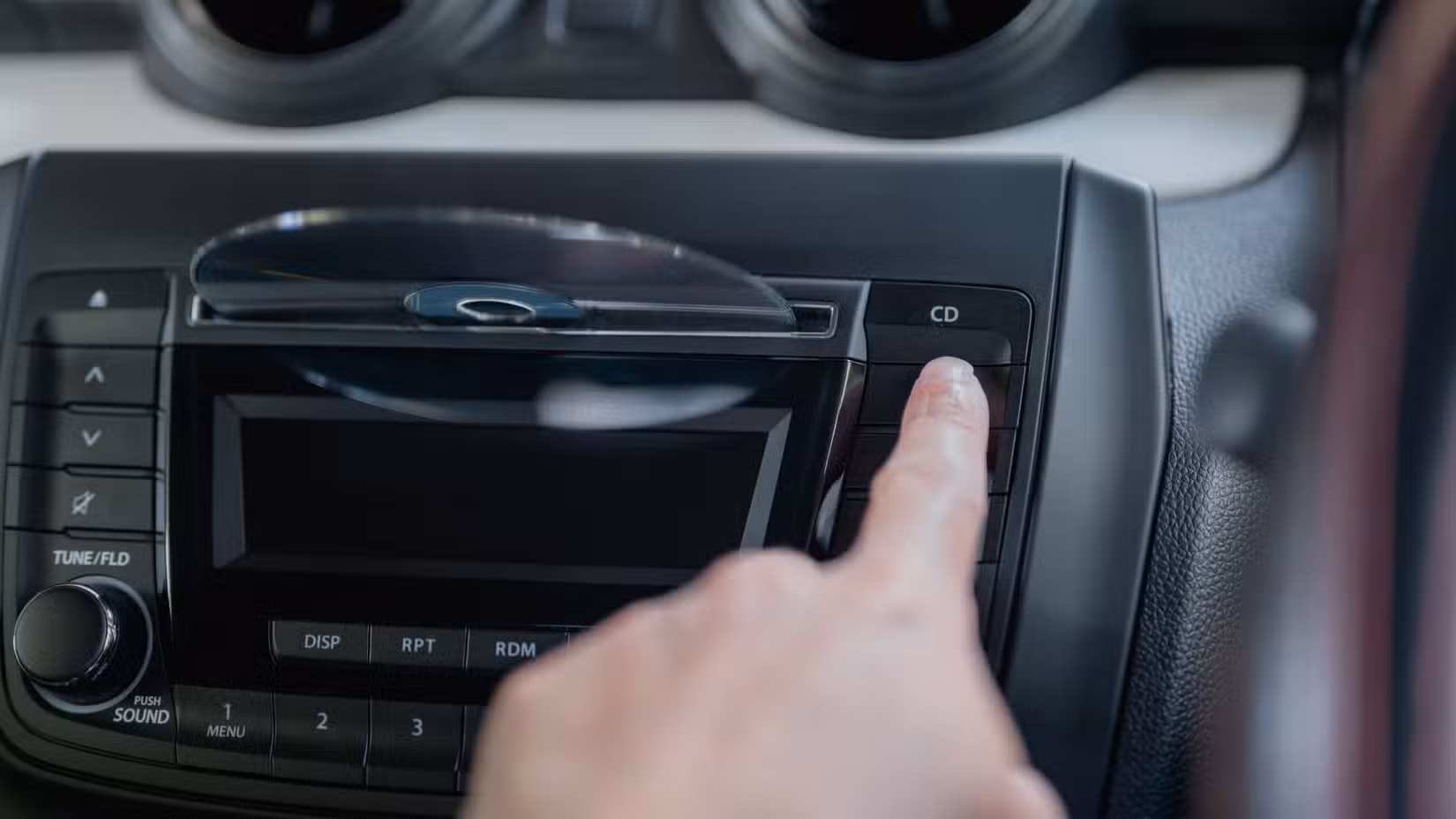 A man pointing his finger at the CD button of an in-car CD player as a disc is being inserted.