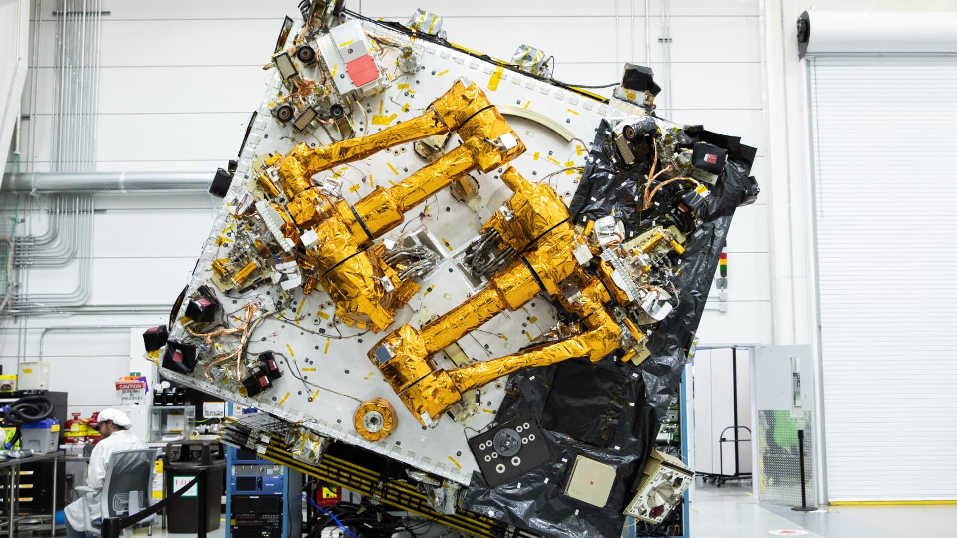 a cube-shaped satellite with two multi-jointed arms inside a cleanroom