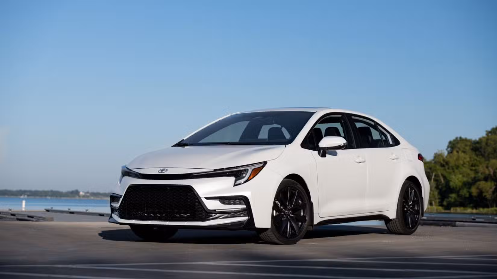 Front 3/4 view of a white 2025 Toyota Corolla Sedan parked with the ocean in the background.