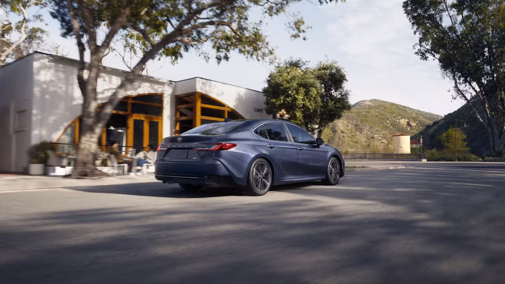 Dynamic rear 3/4 shot of a gray 2026 Toyota Camry driving through a city.