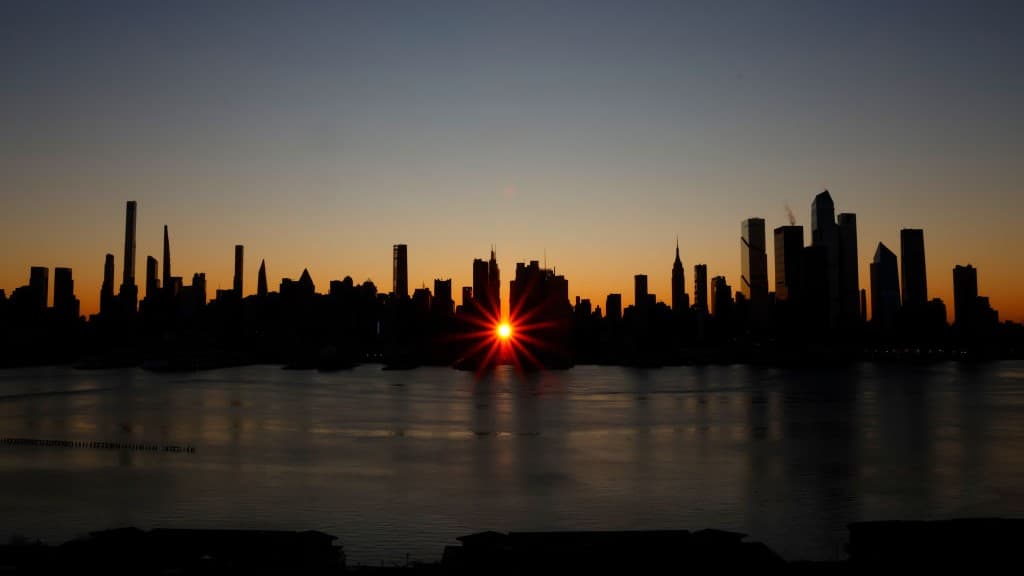 sunrise manhatanhenge with the sun rising between the tall buildings on the new york city skyline.