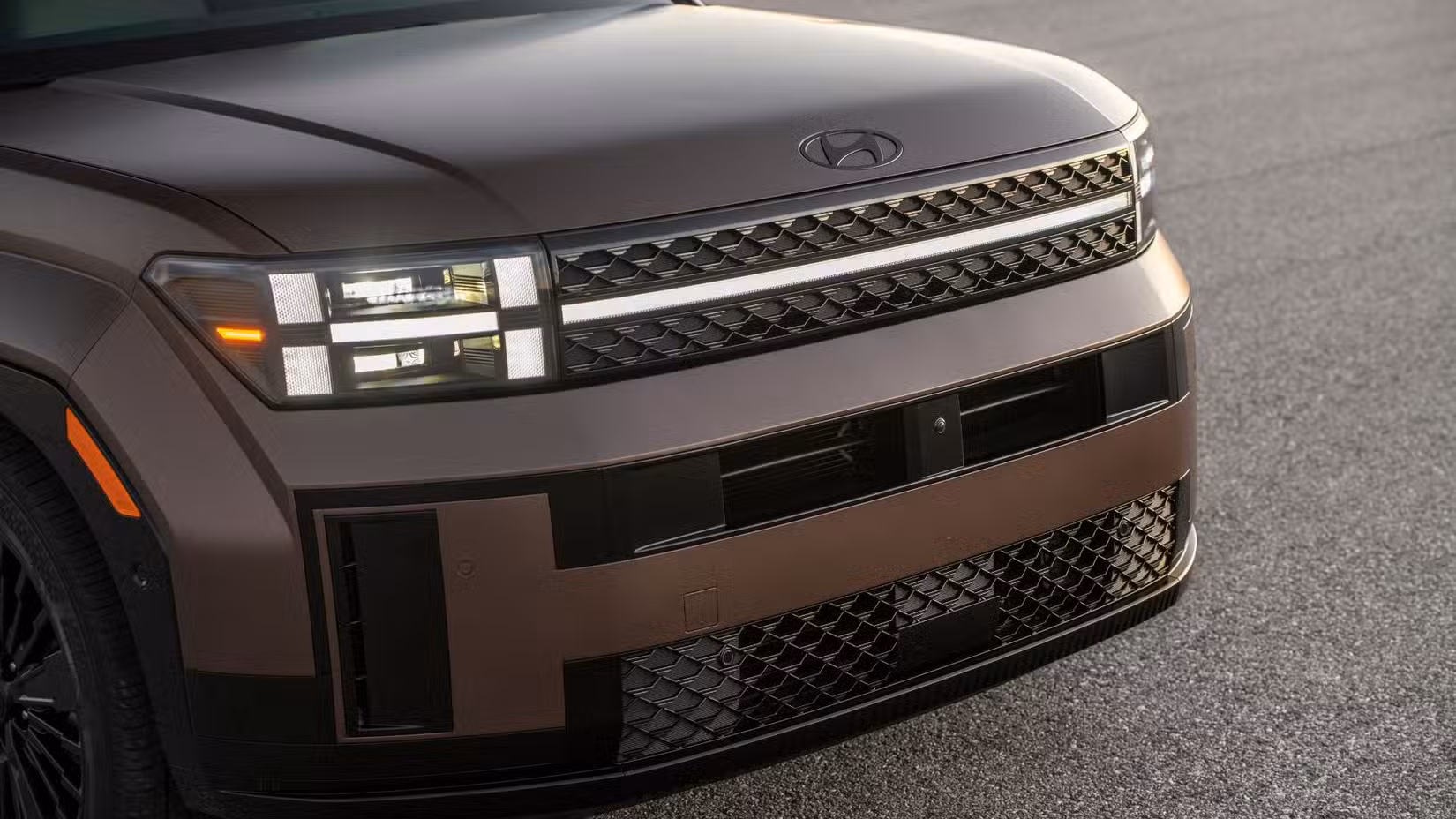 Close-up shot of the frotn end of a bronze 2025 Hyundai Santa Fe Hybrid.