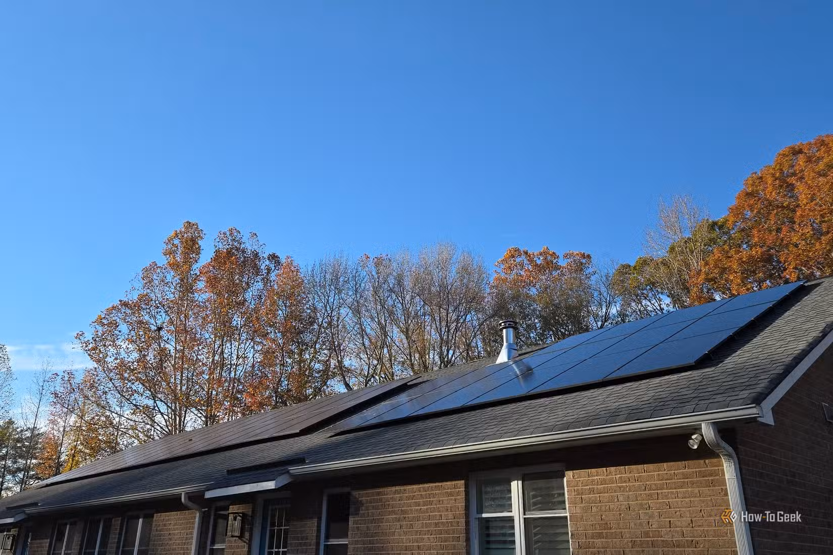 Two solar panel arrays on the roof of a brick home.