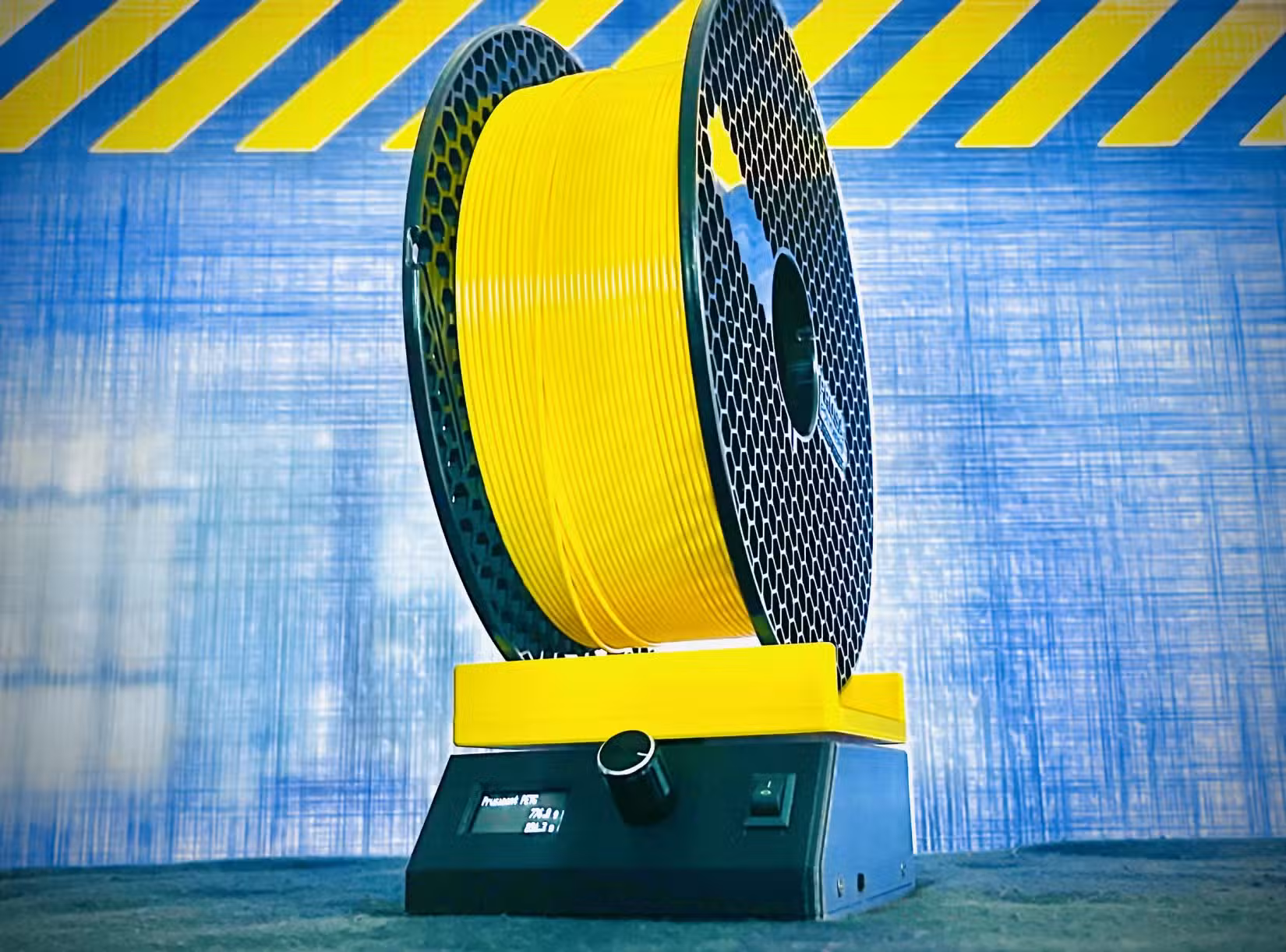 Yellow spool of 3D printer filament mounted on a digital filament scale with a blue industrial-style background.