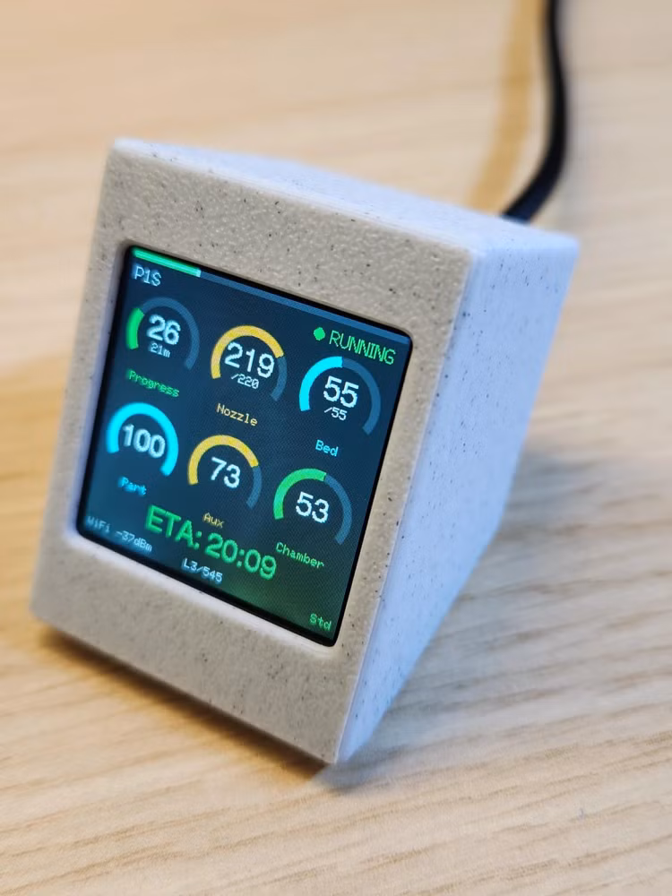 Small 3D-printed desktop display showing real-time 3D printer stats, including nozzle and bed temperatures, print progress, and estimated time remaining.
