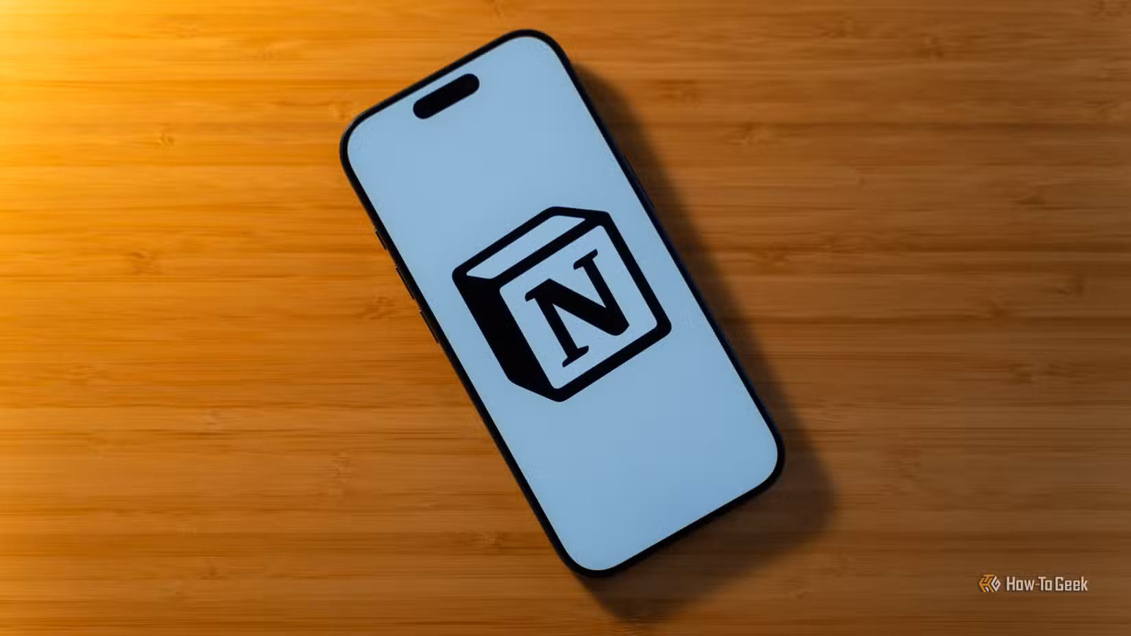 An iPhone 17 Pro with the Notion logo on a white background sitting on a bamboo desk.