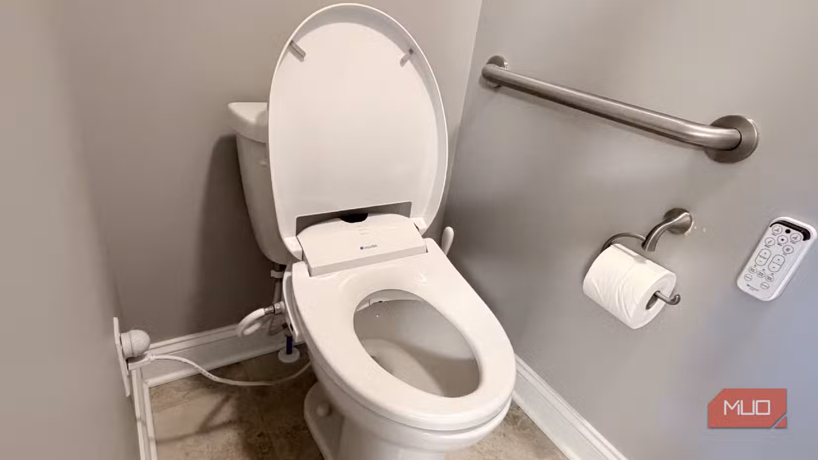 A toilet with toilet paper and a bidet attachment remote next to it