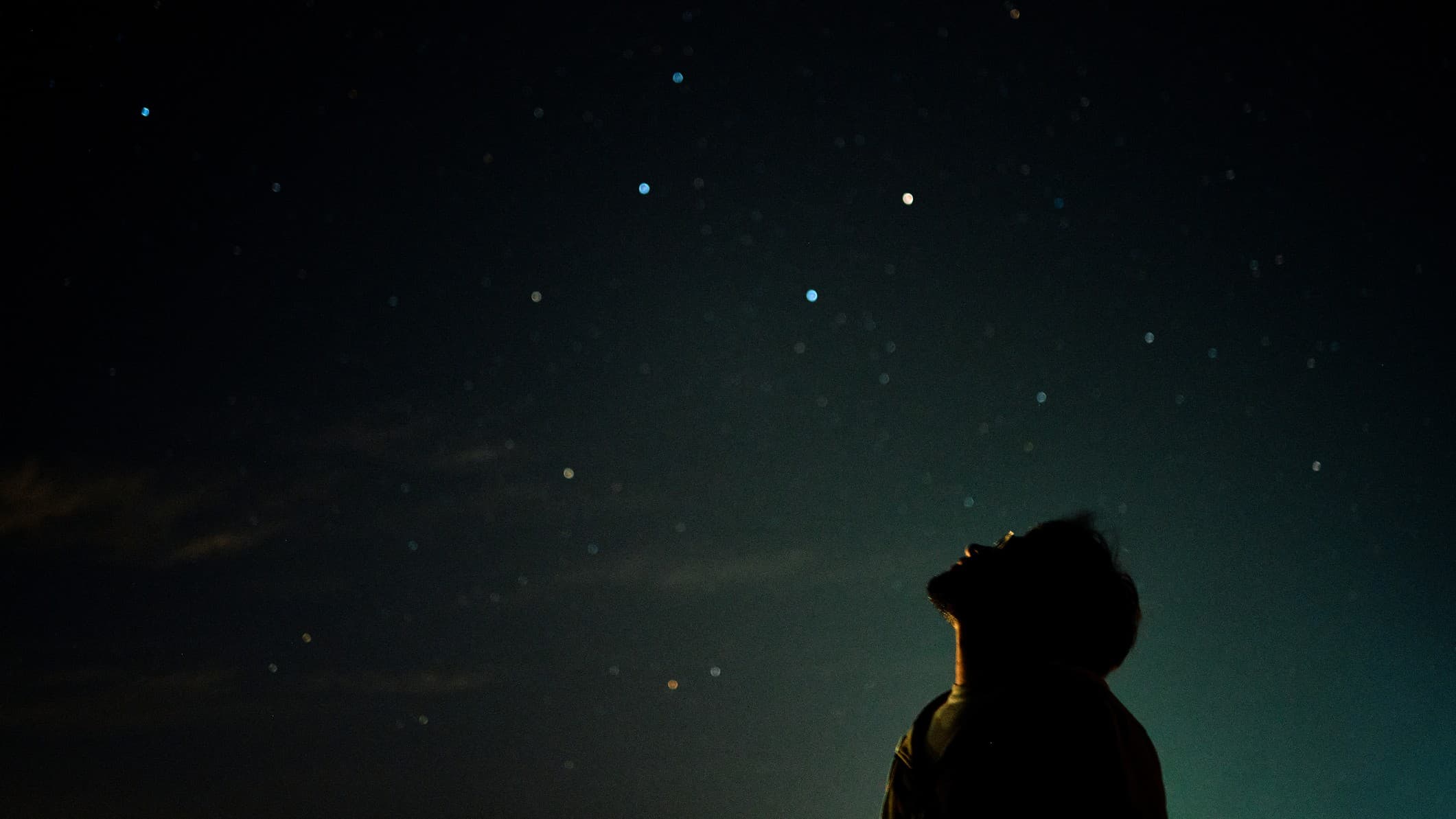 a man looks up at the night sky above.
