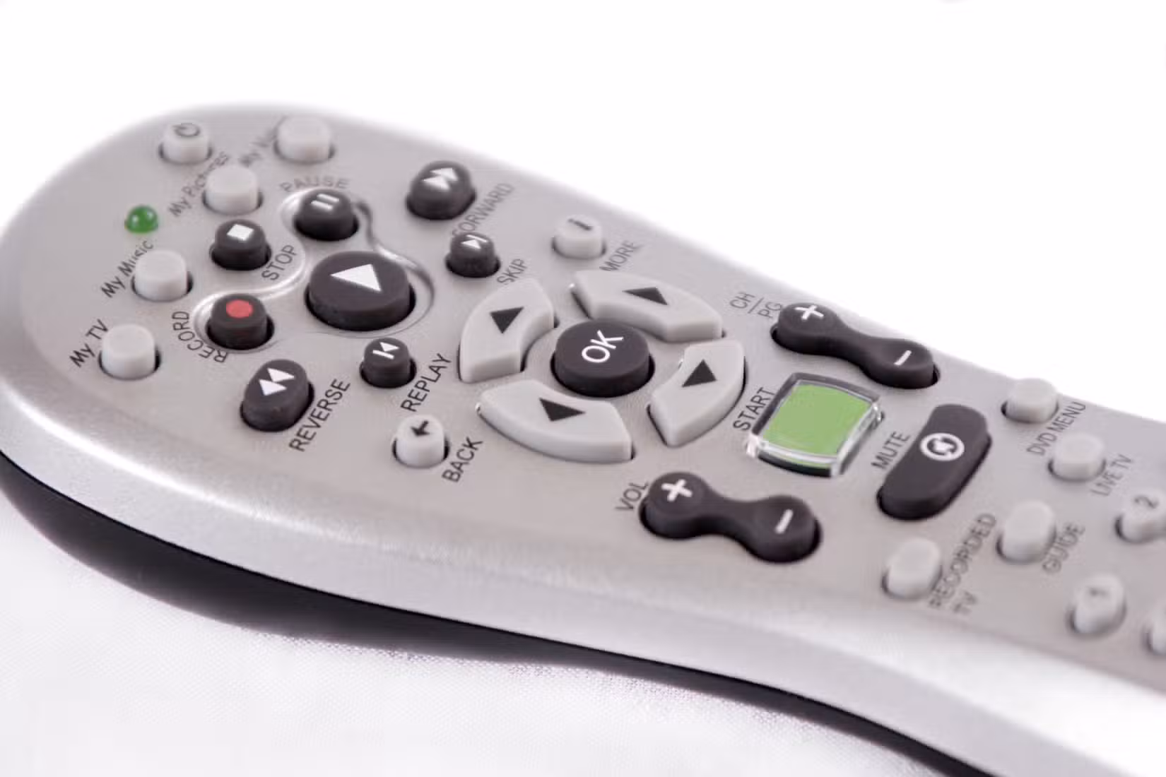 Close-up of a gray TV remote control with numerous labeled buttons, including play, pause, stop, volume, and navigation controls.