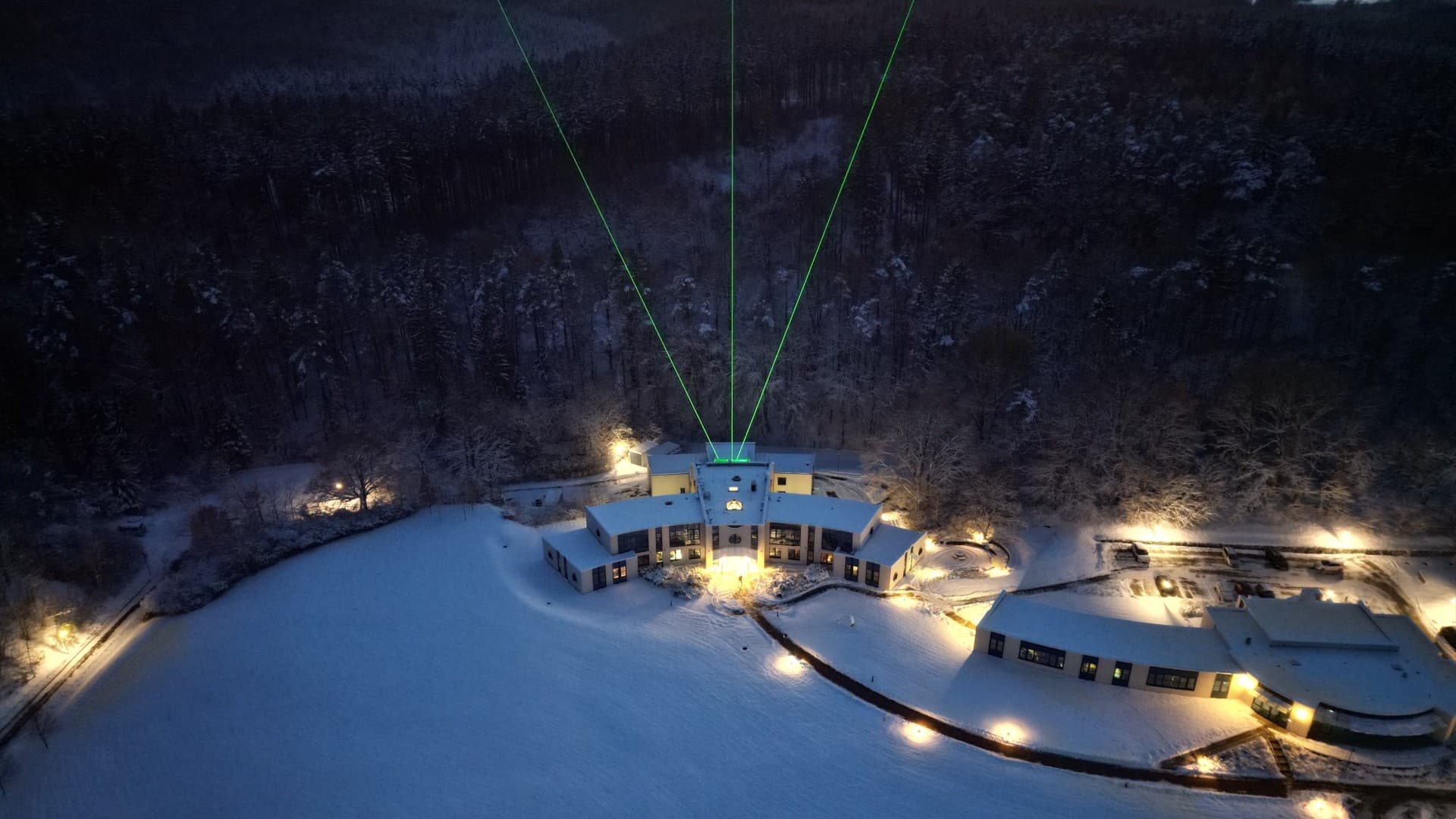 three green beams of light shoot skyward out of a building surrounded by a snowy alpine landscape