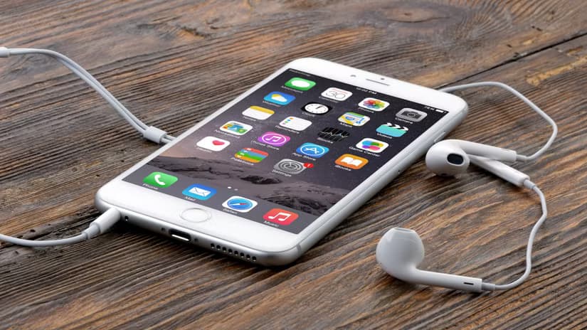 An iPhone 6 Plus on a wooden surface with earbuds connected
