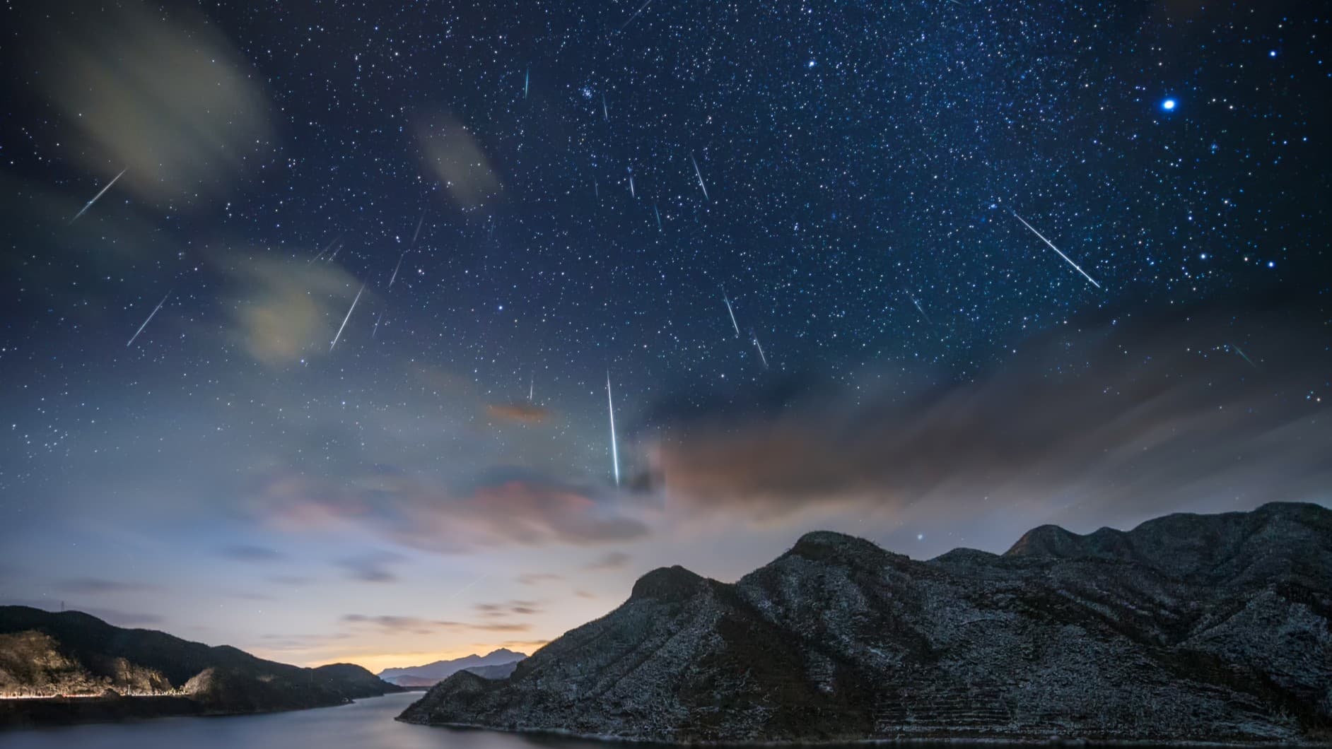streaks of meteor shower bright sparks over mountains and a starry sky.