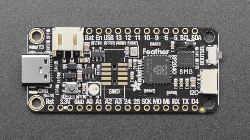 Adafruit's Feather RP2040 laid out on a black surface.