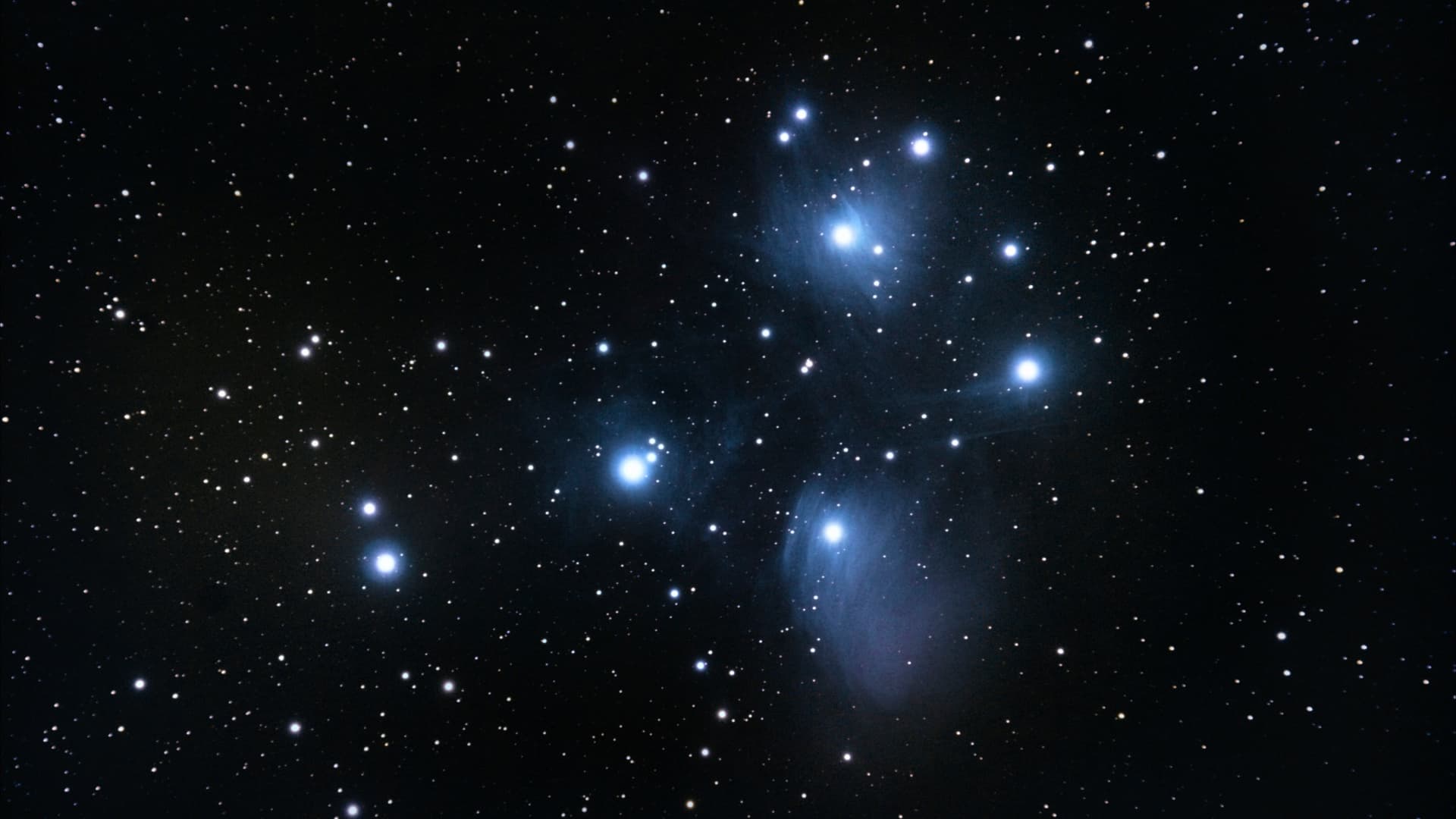 A deep space image showing the seven most prominent blue-white stars of the Pleiades star cluster shining against the blackness of space, with dimmer stars visible beyond.