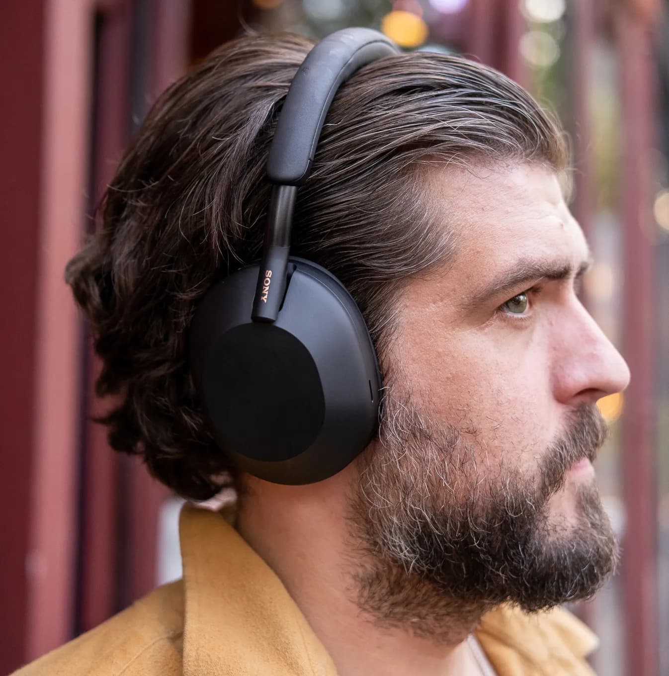 A man wearing Sony’s black WH-1000XM5 noise-canceling headphones outside.