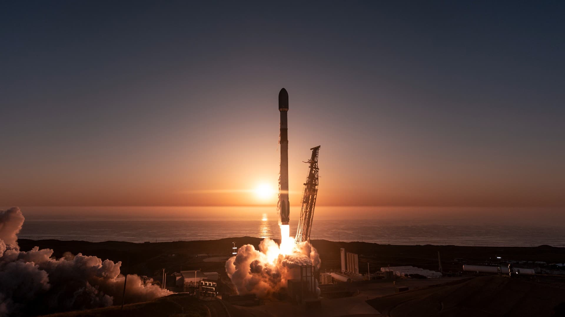 a rocket launches with the sunset over the sea behind it