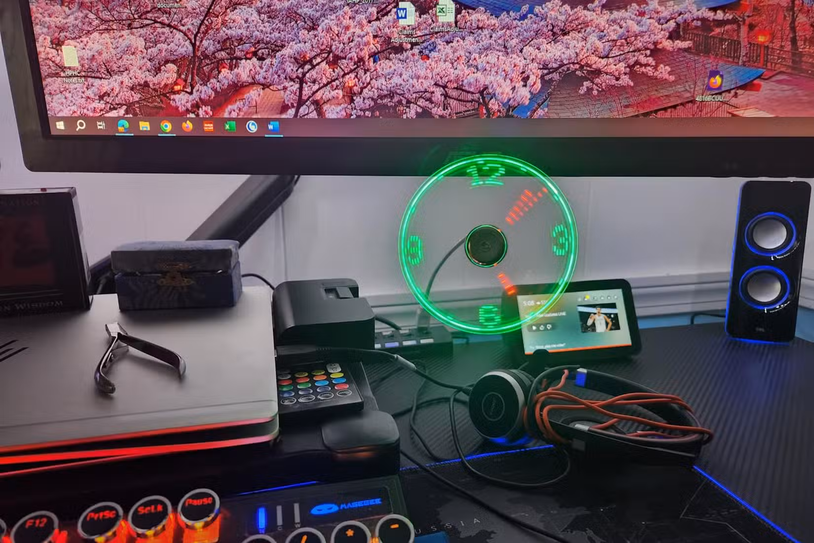 A desk setup featuring a USB fan that displays a green LED clock face.