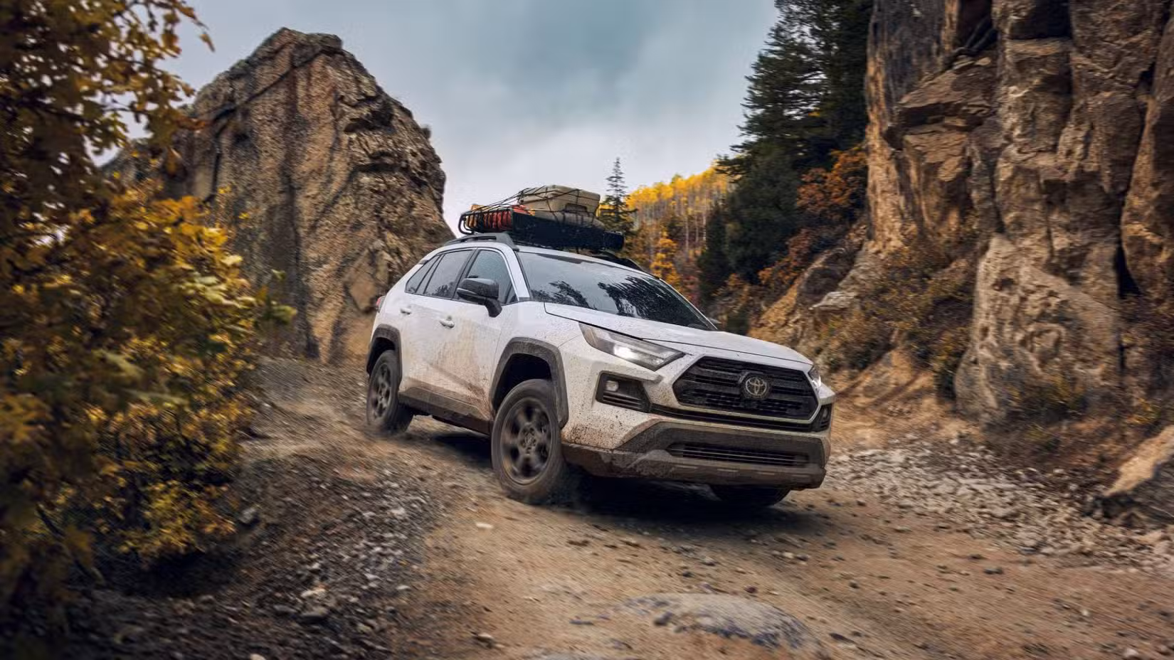Front 3/4 shot of a white 2024 Toyota RAV4 TRD Offroad off-roading with a large rock in the background.