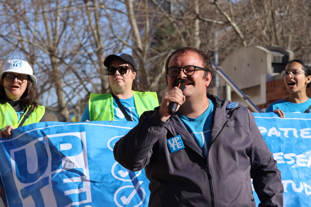 outdoor photo of max belasco standing in front of UPTE banner speaking into a microphone